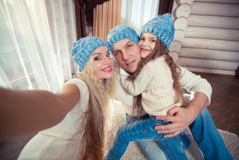 Vakantie, technologie en mensenconcept - de gelukkige familiezitting op vloer en het nemen selfie stellen met smartphone voor bij stock fotografie Vakantie, technologie en mensenconcept - de gelukkige familiezitting op vloer en het nemen selfie stellen met smartphone voor bij stock fotografie