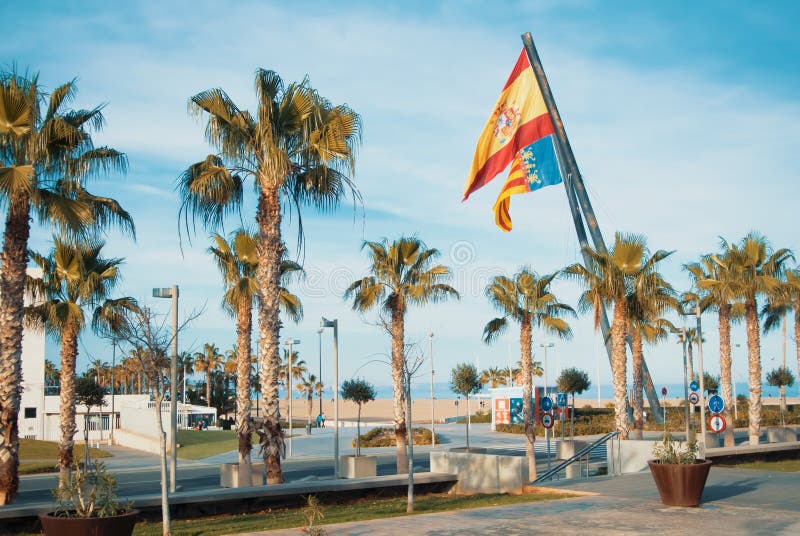 VALENCIA, SPAIN - FEBRUARY 3, 2016: A road to Valencia beach, palms and two big spanish and valencian flags. VALENCIA, SPAIN - FEBRUARY 3, 2016: A road to Valencia beach, palms and two big spanish and valencian flags.