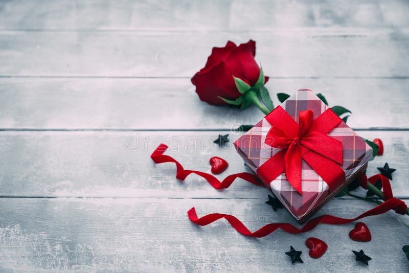 Valentine background with red rose flower and small present box on rustic wood