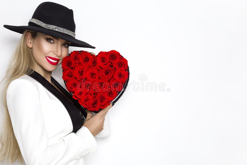 Valentine Beauty, elegant girl with red heart with roses. Portrait of a young female model with gift and hat.