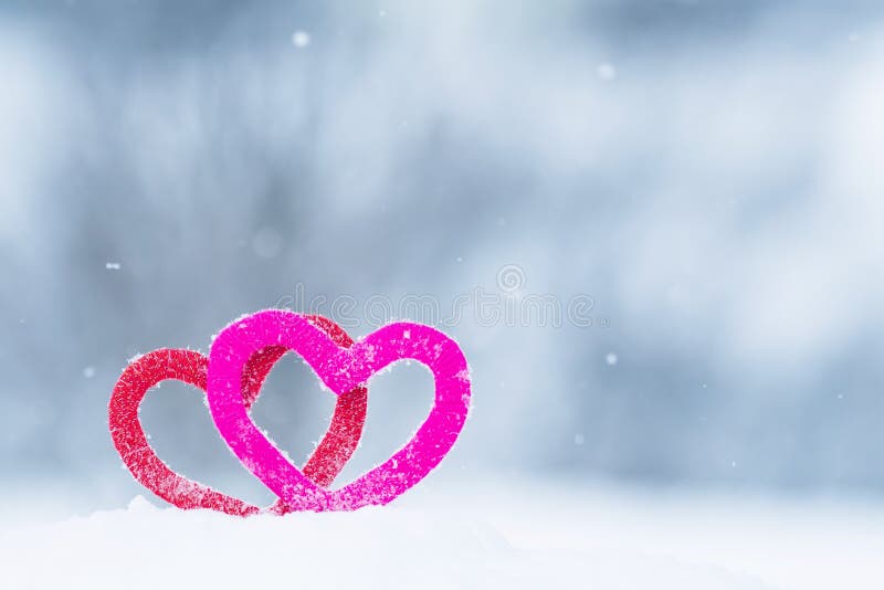 Cute Valentine card with a pair of red and pink knitted decorative elements hearts stand in the snow in the Park