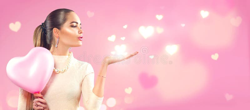 Valentine`s day. Beauty girl with pink heart shaped air balloon pointing hand