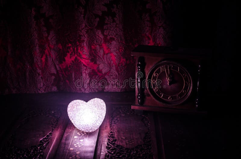 Valentine&x27;s Day composition with sweet burning multicolored heart on dark background and old vintage clock, time and love