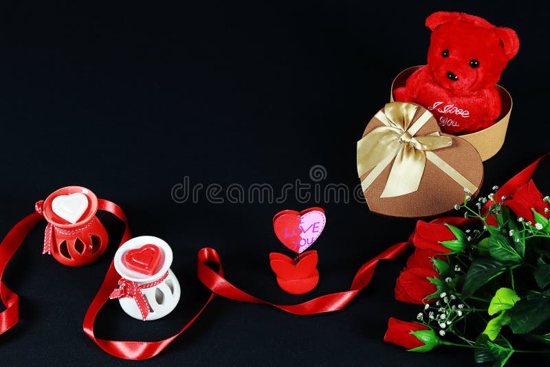 Valentine`s day concept. Teddy bear in heart shaped gift box with candle and red roses on black background.