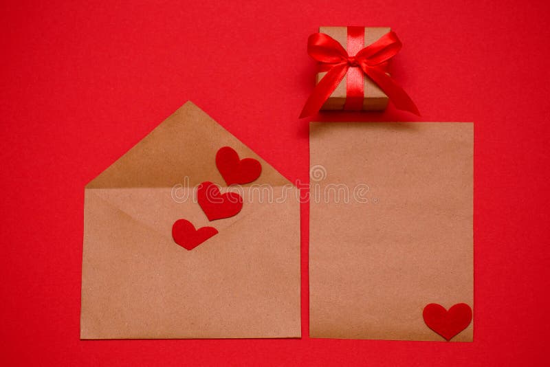 Valentine`s Day, February 14 - an envelope with red hearts and a sheet for the record on a red background, a gift tied with a red stock photo Valentine`s Day, February 14 - an envelope with red hearts and a sheet for the record on a red background, a gift tied with a red stock photo