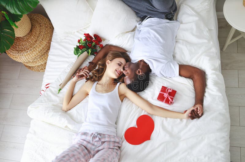 Valentine`s Day. happy couple with flowers in bed