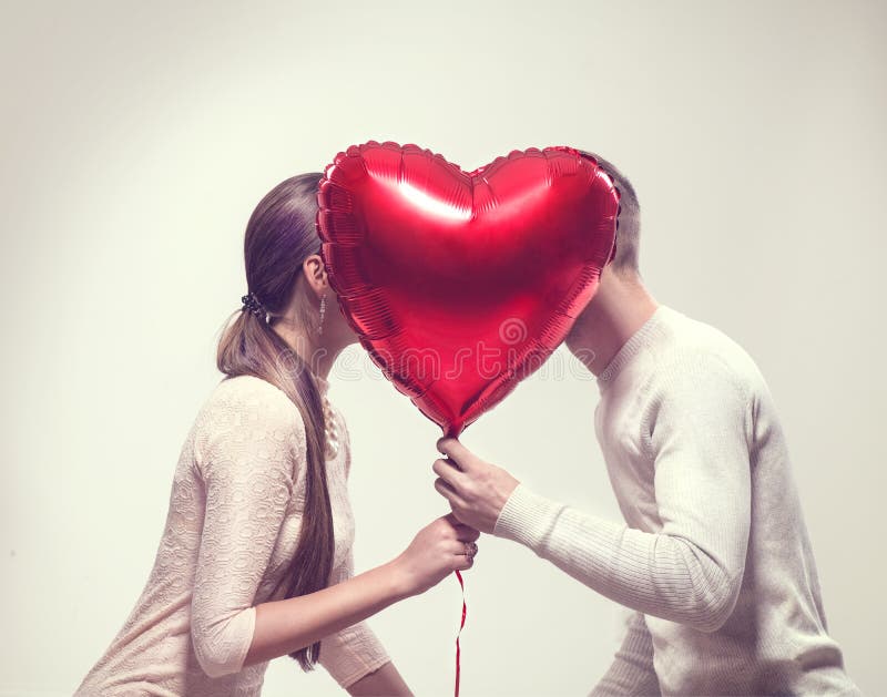 Valentine`s day. Happy joyful couple holding heart shaped air balloon and kissing