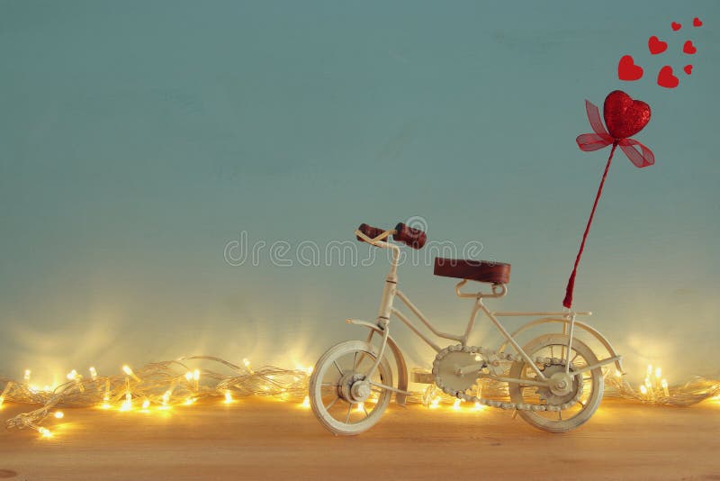 Valentine& x27;s day romantic background with white vintage bicycle toy and glitter red heart on it over wooden table.