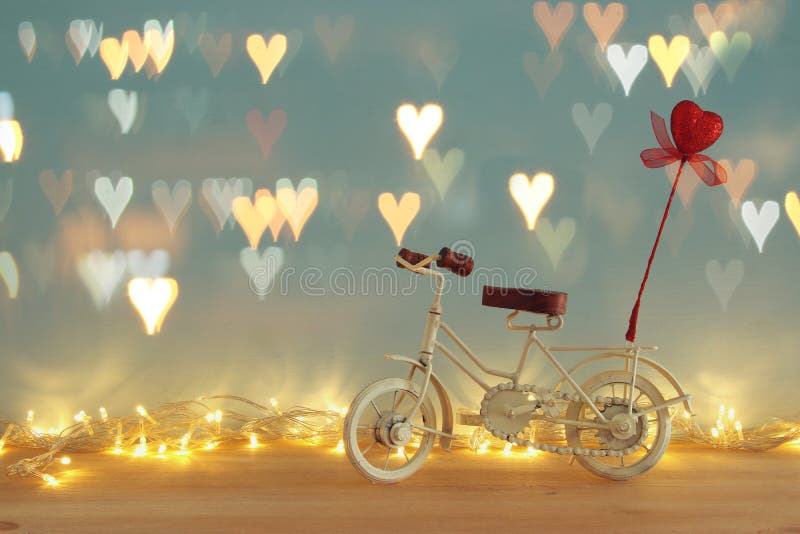 Valentine& x27;s day romantic background with white vintage bicycle toy and glitter red heart on it over wooden table.