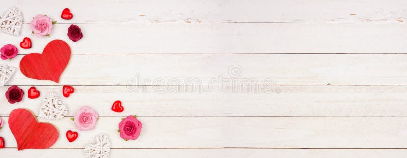 Valentines Day banner with corner border of hearts, flowers and decor against a white wood background with copy space