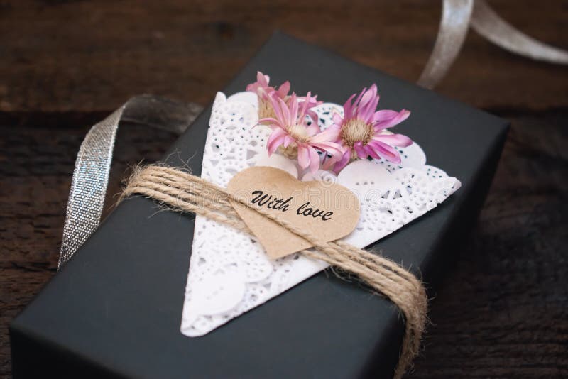 Valentines day gift box ideas. Black paper present box text WITH LOVE on heart, lace napkin, jute rope and silver on dark stock image Valentines day gift box ideas. Black paper present box text WITH LOVE on heart, lace napkin, jute rope and silver on dark stock image
