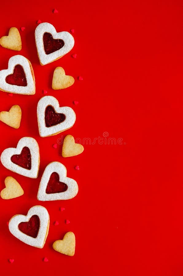 Valentines day food background. Heart shaped Linzer cookies with jam and icing sugar on a red background.