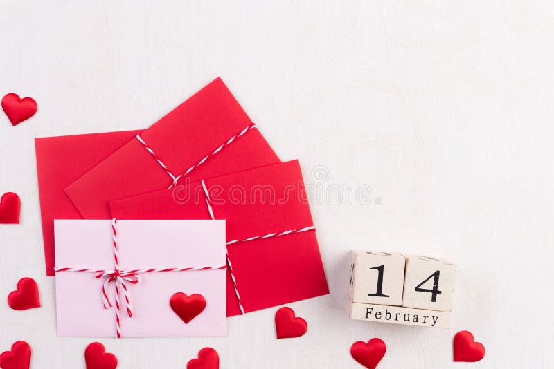 Valentines day and love concept. Red hearts and red pink letter cover and February 14 text on wooden block on white wooden background.