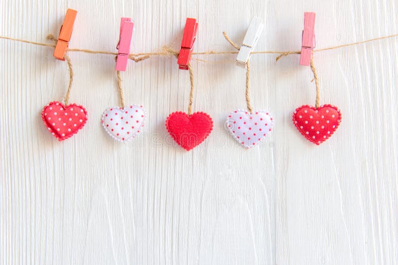 Valentine’s Day. Sewed pillow hearts row border on red, pink and white clothespins at rustic white wood planks royalty free stock image Valentine’s Day. Sewed pillow hearts row border on red, pink and white clothespins at rustic white wood planks royalty free stock image