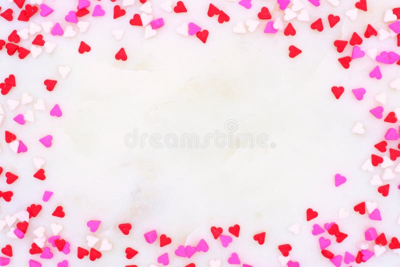 Valentinsgruß-Tagessüßigkeitsherz besprüht Rahmen über einem weißen strukturierten Hintergrund