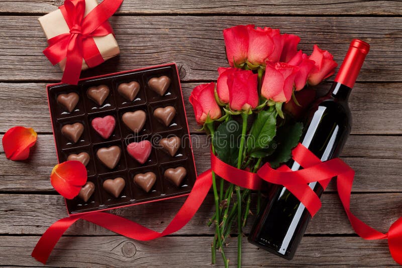Valentines day with red roses, wine bottle and chocolate box on wooden table. Top view. Valentines day with red roses, wine bottle and chocolate box on wooden table. Top view