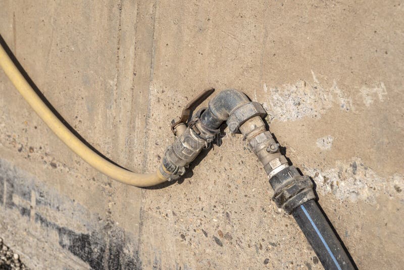 Old water valve connected to a hose, in the factory installed outside by the wall. Old water valve connected to a hose, in the factory installed outside by the wall