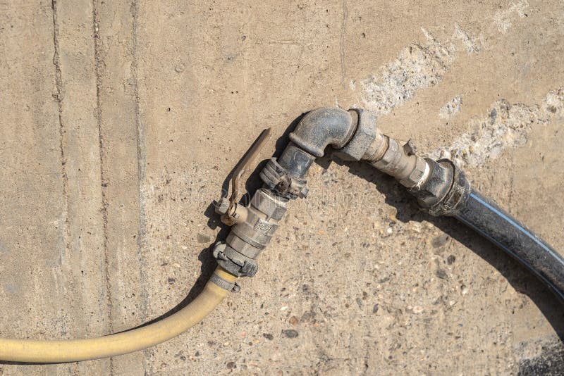 Old water valve connected to a hose, in the factory installed outside by the wall. Old water valve connected to a hose, in the factory installed outside by the wall