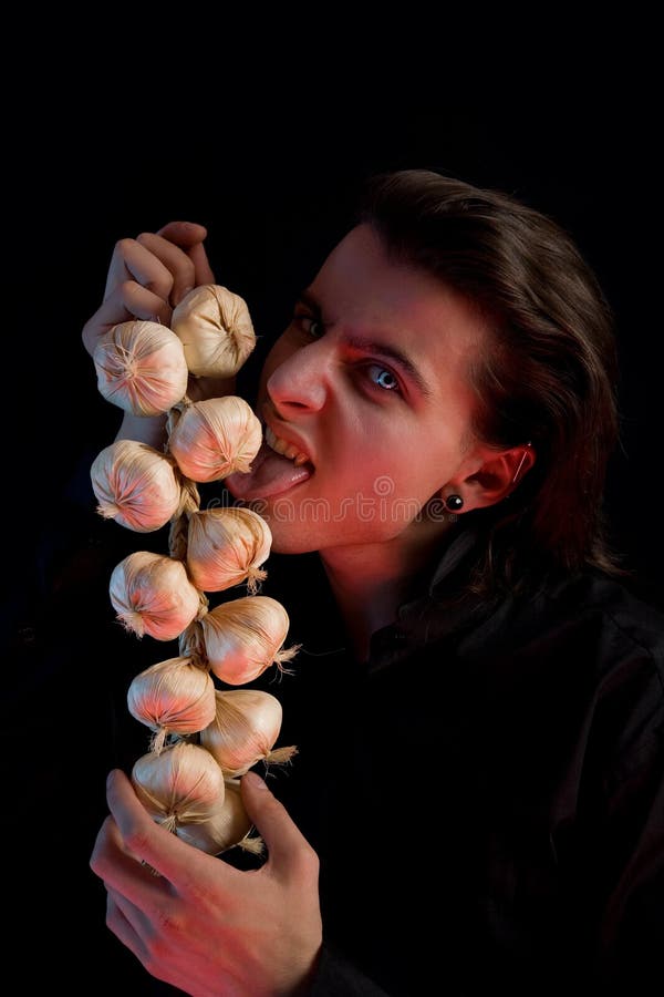 Vampire with scary eyes is licking garlic stock image
