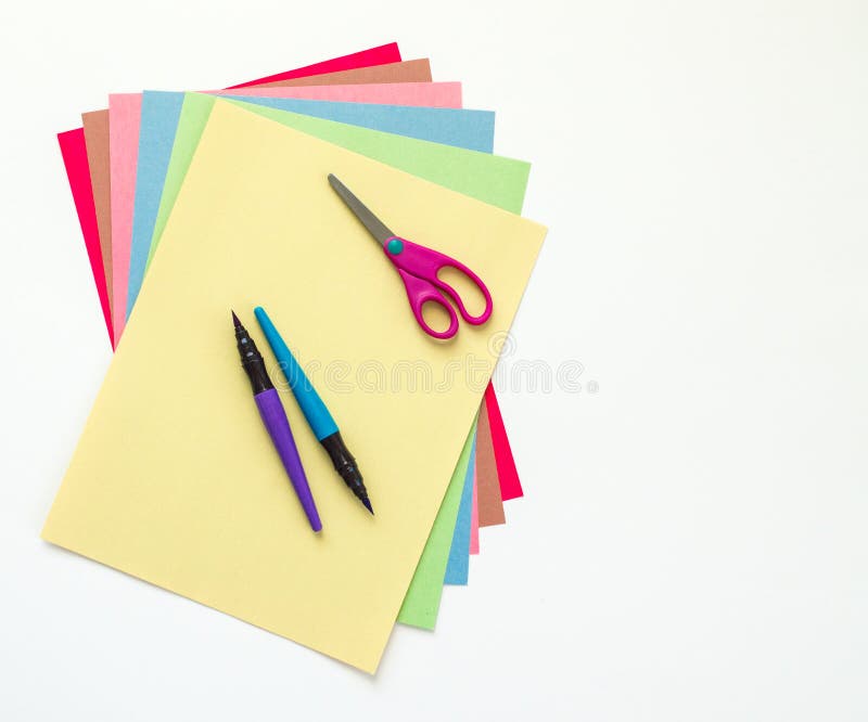 Back to school-child`s magenta scissors and two paint pens on top of multicolored fanned out construction paper isolated on white. Back to school-child`s magenta scissors and two paint pens on top of multicolored fanned out construction paper isolated on white