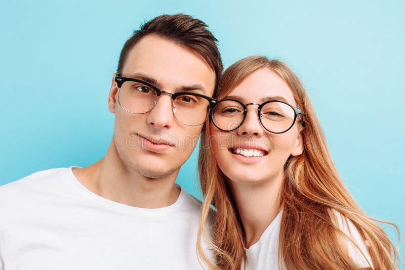 Van een jong gelukkig paar, die glazen, de mens en vrouw, het glimlachen dragen, die de camera onderzoeken, tegen een blauwe acht stock foto Van een jong gelukkig paar, die glazen, de mens en vrouw, het glimlachen dragen, die de camera onderzoeken, tegen een blauwe acht stock foto