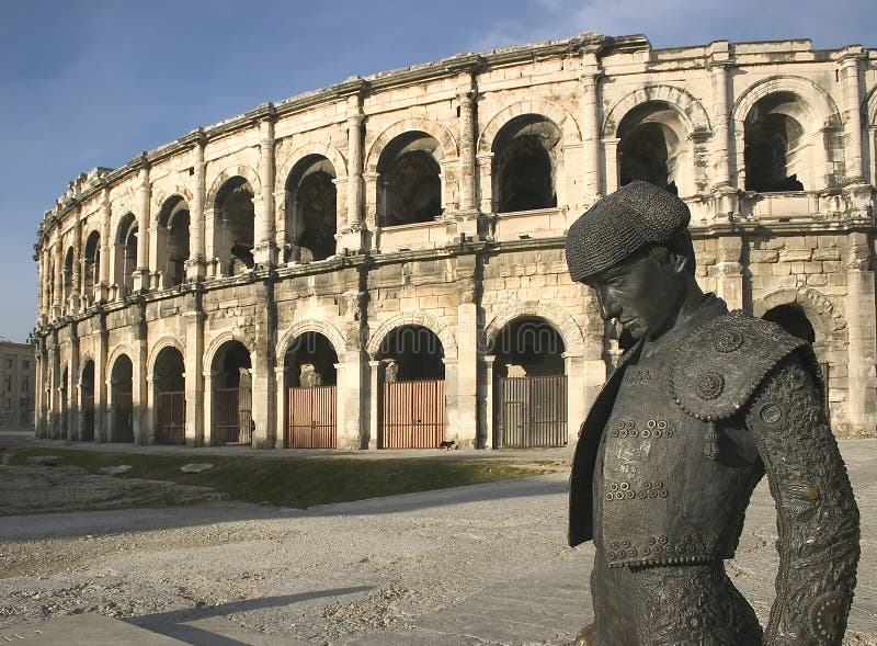 A view of the roman Arena in NÃ®mes, France, Europe, on the foreground bronze statue of a famous local toreador. A view of the roman Arena in NÃ®mes, France, Europe, on the foreground bronze statue of a famous local toreador
