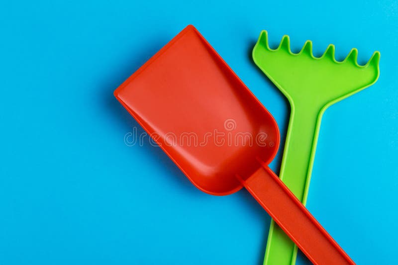 Vanga variopinta e rastrello del giocattolo su fondo blu luminoso fotografia stock Vanga variopinta e rastrello del giocattolo su fondo blu luminoso fotografia stock