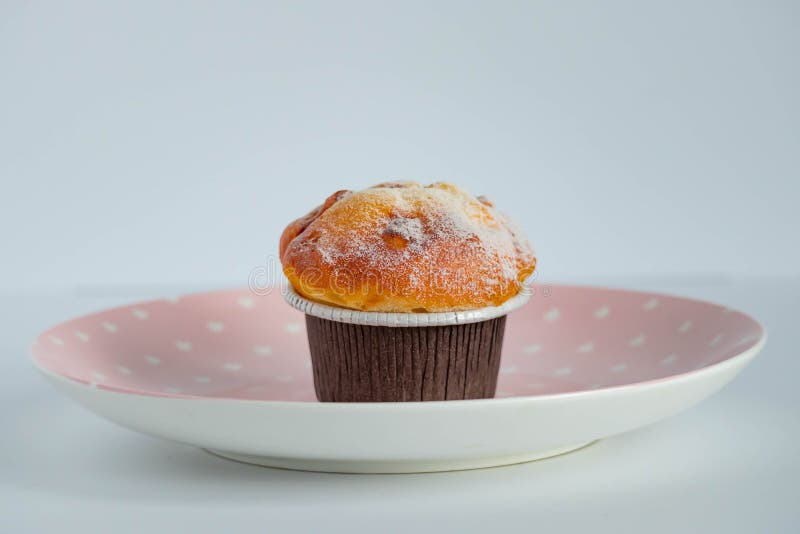 Vanilla Cupcake in Brown Paper Liners Placed on a Pink Dish. Side View