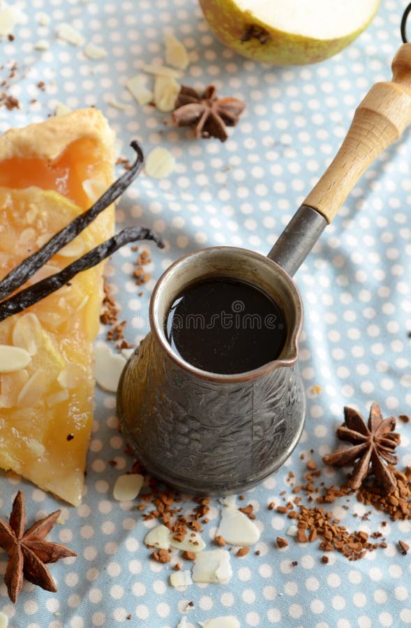 Vanilla coffee in the traditional cezve with a piece of pear cake, decorated with almond and vanilla pod. Vanilla coffee in the traditional cezve with a piece of pear cake, decorated with almond and vanilla pod