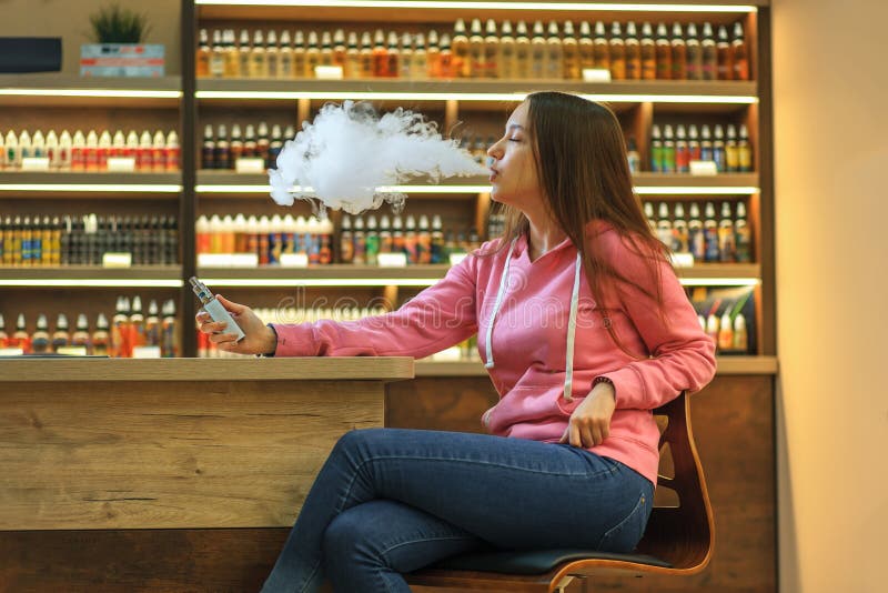 Vape kobieta Młoda śliczna dziewczyna dymi elektronicznego papieros w różowym hoodie zdjęcie stock Vape kobieta Młoda śliczna dziewczyna dymi elektronicznego papieros w różowym hoodie zdjęcie stock