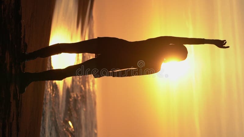 Vapen från silhuette-kvinna som upphöjts på sandstranden vid soluppgång på solskiva i bakgrunden som stiger över horisonten