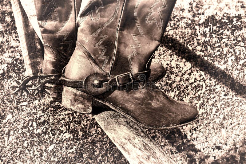 American West rodeo traditional leather cowboy boots with western antique spurs resting on an old wood fence rail at a ranch corral during a vintage round-up. American West rodeo traditional leather cowboy boots with western antique spurs resting on an old wood fence rail at a ranch corral during a vintage round-up