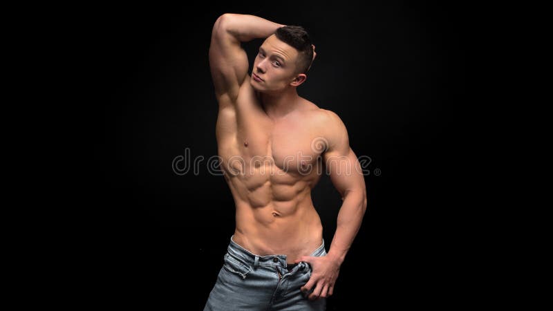 Vaqueros que llevan descamisados del hombre muscular joven hermoso, en fondo oscuro en tiro del estudio fotografía de archivo libre de regalías Vaqueros que llevan descamisados del hombre muscular joven hermoso, en fondo oscuro en tiro del estudio fotografía de archivo libre de regalías