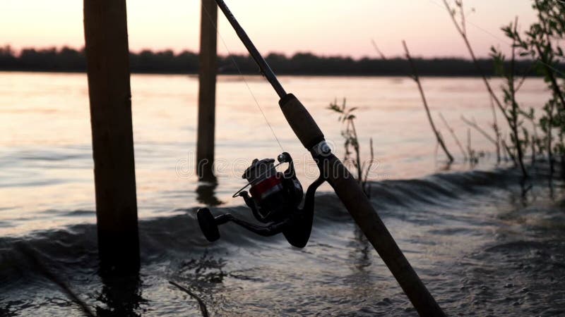 Vara de pesca com mordida de espera do carretel no por do sol da noite do fundo no rio