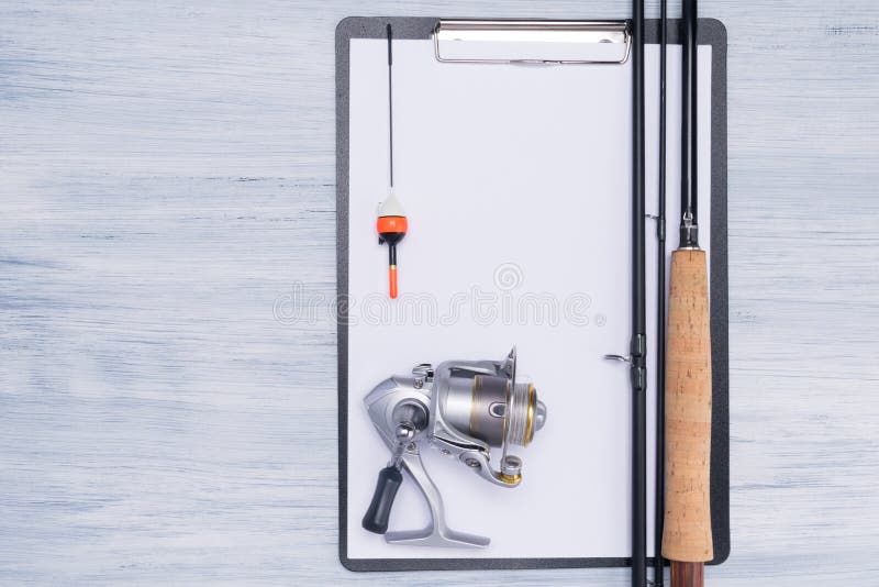 Vara de pesca com o carretel para pescar e uma tabuleta limpa para notas em um fundo claro foto de stock royalty free Vara de pesca com o carretel para pescar e uma tabuleta limpa para notas em um fundo claro foto de stock royalty free