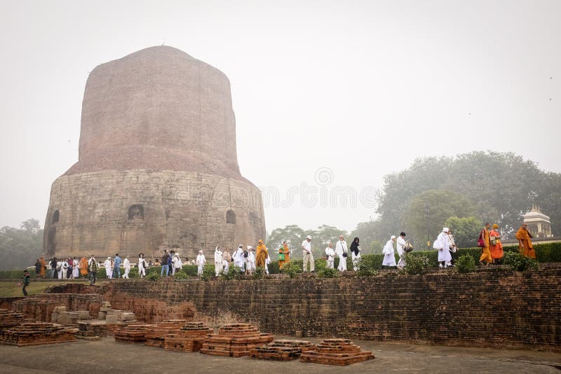 VARANASI, INDIA - DECEMBER 2, 2016: Buddhist monks and tourists come to visit and pray in the misty morning at Dhamekh Stupa, the