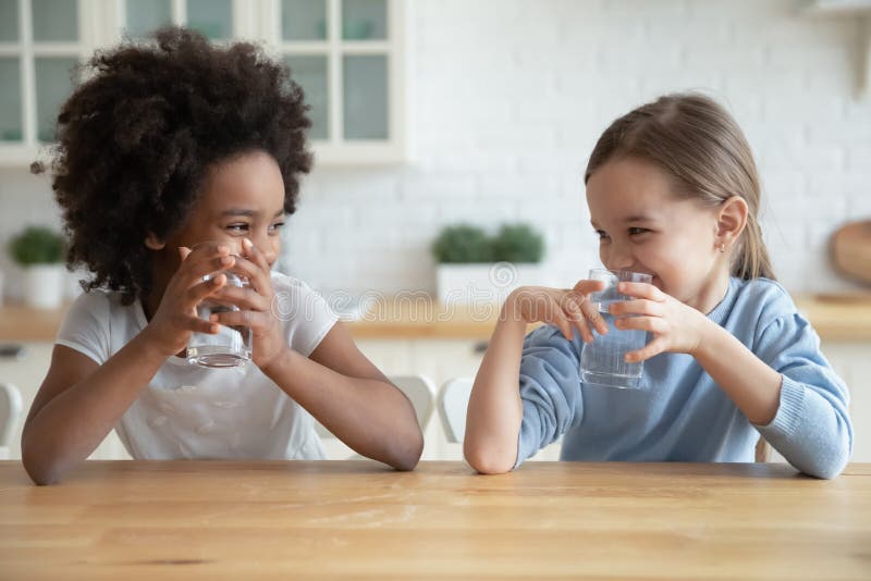 Varias niñas lindas sonrientes que beben agua dulce en cocina imagen de archivo