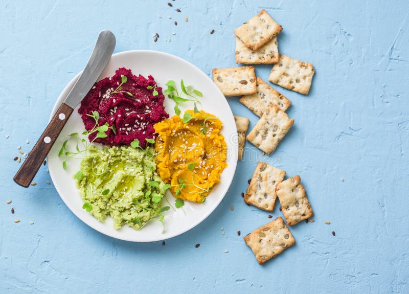 Variations of hummus and crackers. Pumpkin, turmeric, avocado, beetroot hummus with olive oil, sesame seeds and micro greens on a