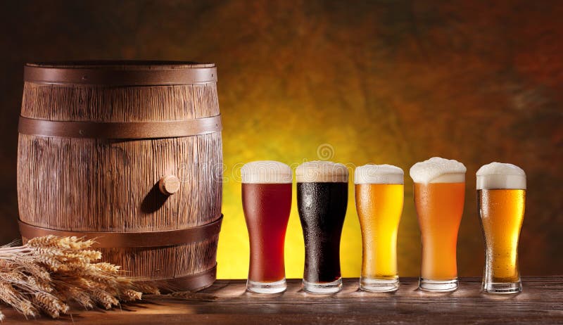 Assortment of beer glasses with a wooden barrel. Background - dark yellow gradient. Assortment of beer glasses with a wooden barrel. Background - dark yellow gradient.