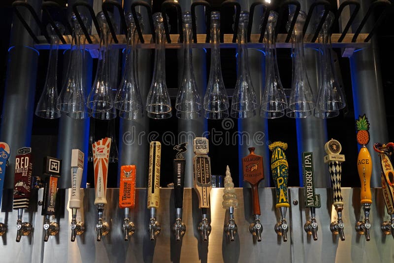Los Angeles, California, USA - Sept. 15, 2023: A variety of beer tap handle logos are shown on display at a bar, with half yard beer glasses hanging above. For editorial uses only. Los Angeles, California, USA - Sept. 15, 2023: A variety of beer tap handle logos are shown on display at a bar, with half yard beer glasses hanging above. For editorial uses only.