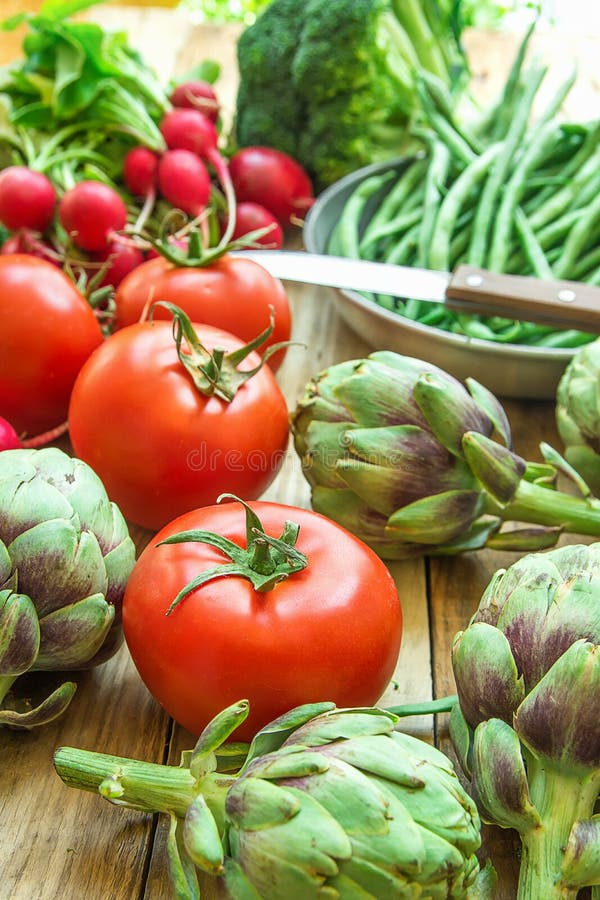 Variety of Fresh Organic Vegetables Artichokes Green Beans Tomatoes Red Radish Broccoli on Wood Garden Kitchen Table Vegan