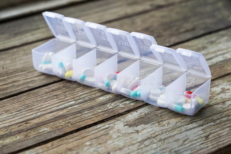 Varietà di pillole nell'organizzatore di plastica bianco della pillola su legno stagionato fotografia stock Varietà di pillole nell'organizzatore di plastica bianco della pillola su legno stagionato fotografia stock