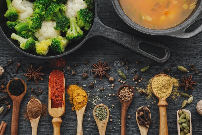 Various aromatic colorful spices and herbs in wooden spoons and scoops. Broccoli and cauliflower on iron frying pan.