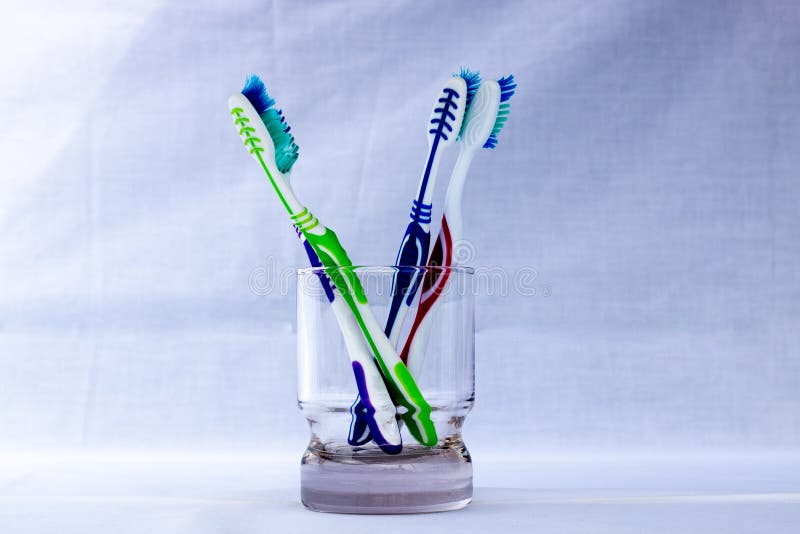 Various Colored Toothbrushes in a Transparent Glass Cup with a White