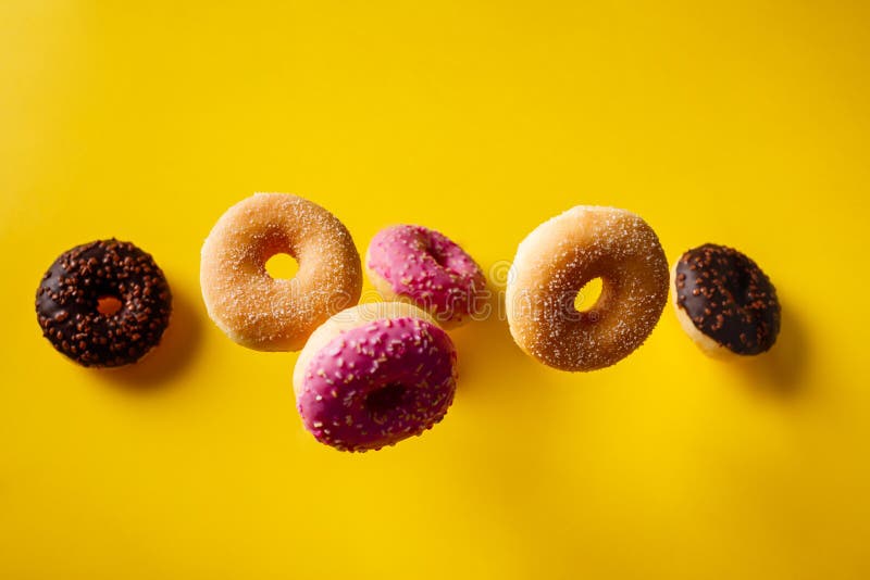 Various decorated doughnuts in motion falling on yelloy background