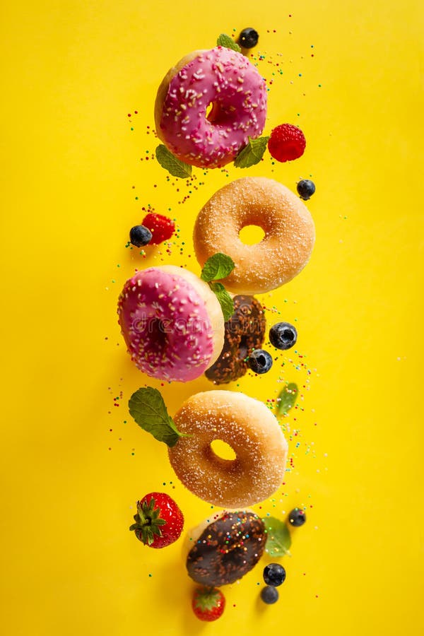 Various decorated doughnuts with sprinkles and berries in motion falling on yelloy background