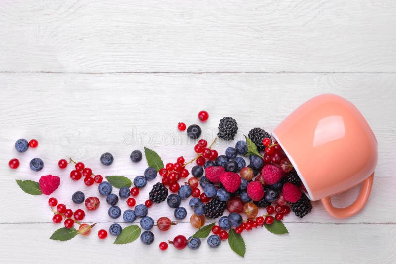 Various fresh berries close-up including blueberries, raspberries, blackberries currants and gooseberries drop out of a cup on a w