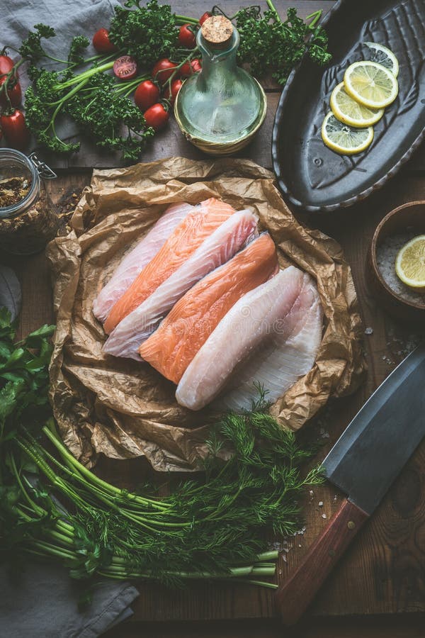 Various of fresh raw fish fillets on kitchen table background with herbs, spices and lemon slices. Colorful raw fish selection.