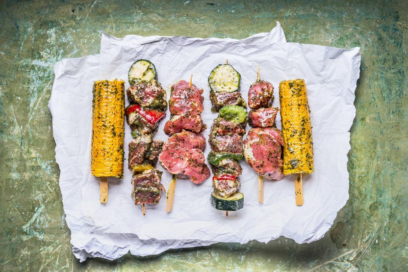 Various Meat Skewers for grill with vegetables , corn ears and condiment on green rustic background royalty free stock photo