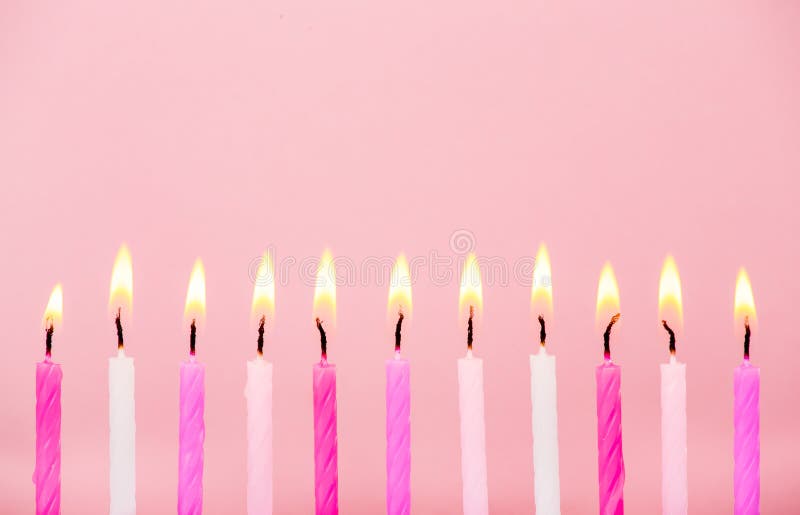 Various pink color birthday cake candles burning in line on pastel pink background.